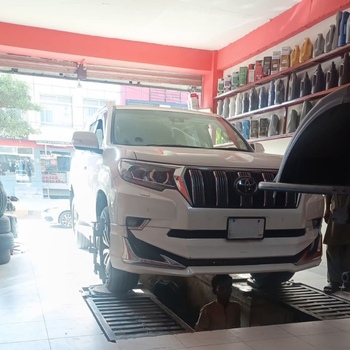 White SUV on lift in auto workshop with mechanic underneath.