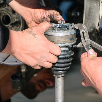 Auto mechanic inspecting and repairing a vehicle suspension strut assembly.
